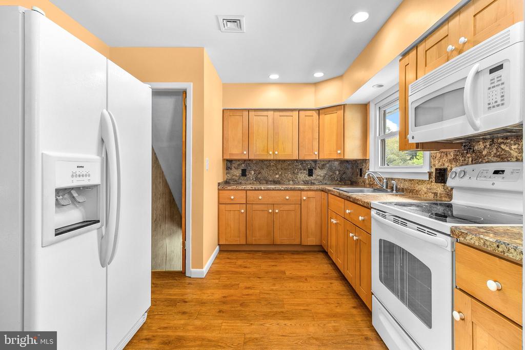 Kitchen with wood cabinets, granite counters, hardwood floors, and white appliances.