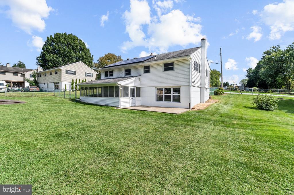White two-story house with an enclosed sunroom and patio overlooking a broad lawn.