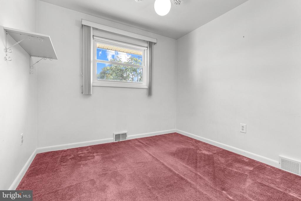 Empty bedroom with pink carpet and a high window overlooking trees.