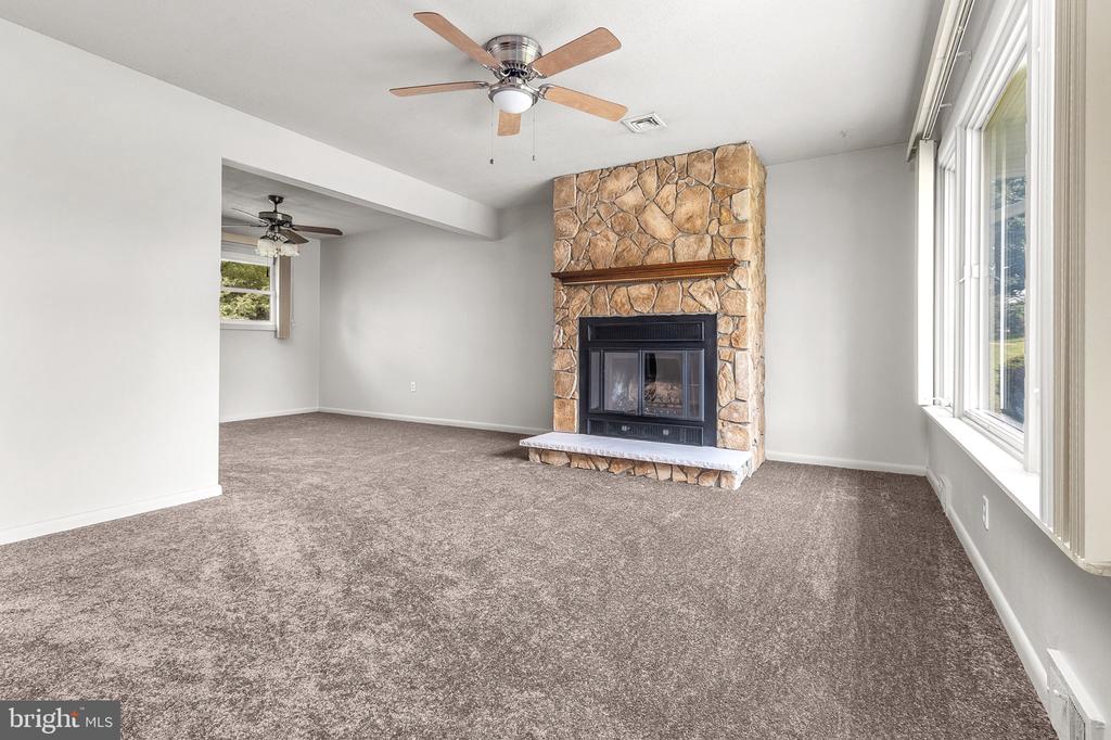 Vacant living room with a stone fireplace, gray carpet, and large windows.