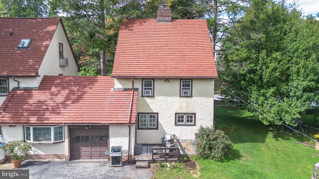 Two-story stucco house with red shingle roofs, attached garage, and small deck beside a green lawn.