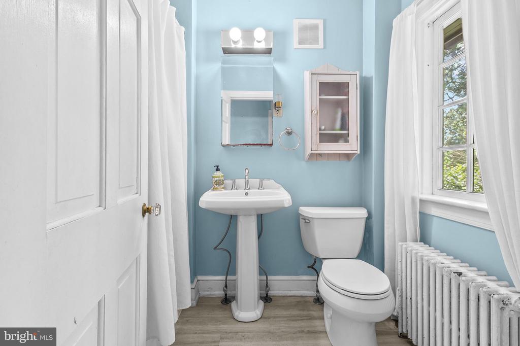 Bathroom with blue walls, a pedestal sink, white toilet, and tall curtained window.