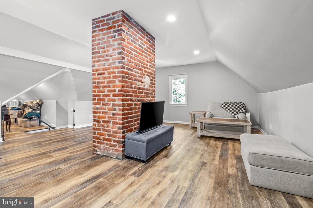 Attic living area with a central brick chimney, sloped ceiling, and gray seating.