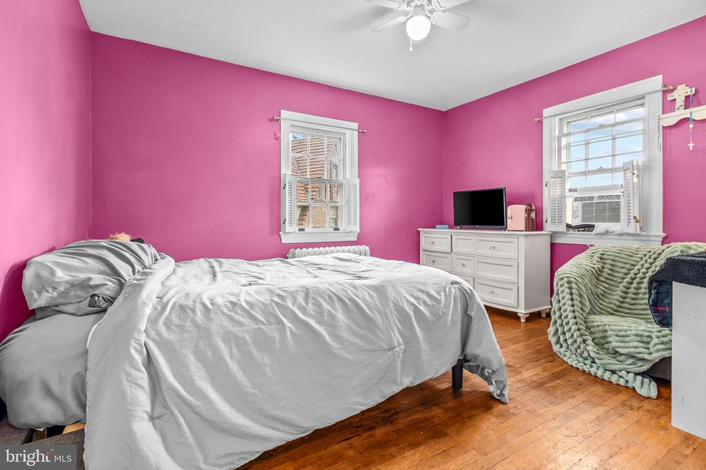 Bedroom with vivid pink walls, a white bed, hardwood floors, and a green throw on a chair.