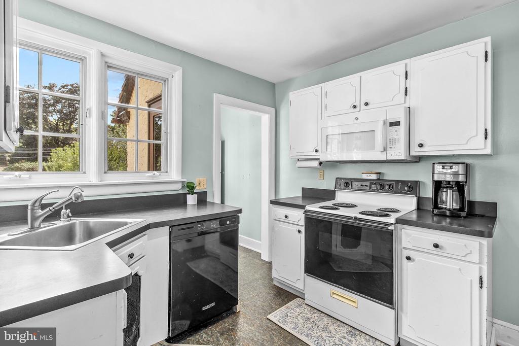 Kitchen with pale blue-green walls, white cabinets, dark countertops, and two large windows.