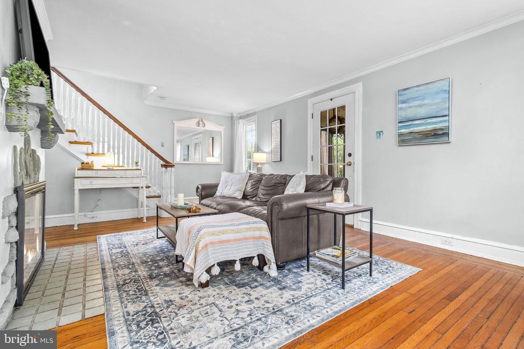 Living room with a leather sofa, patterned rug, hardwood floors, and staircase beside the fireplace.
