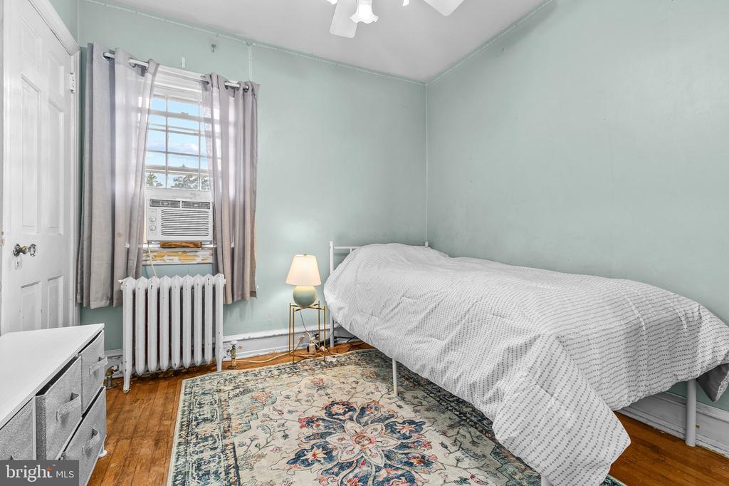 Bedroom with pale green walls, a white bed, patterned rug, and window air conditioner.