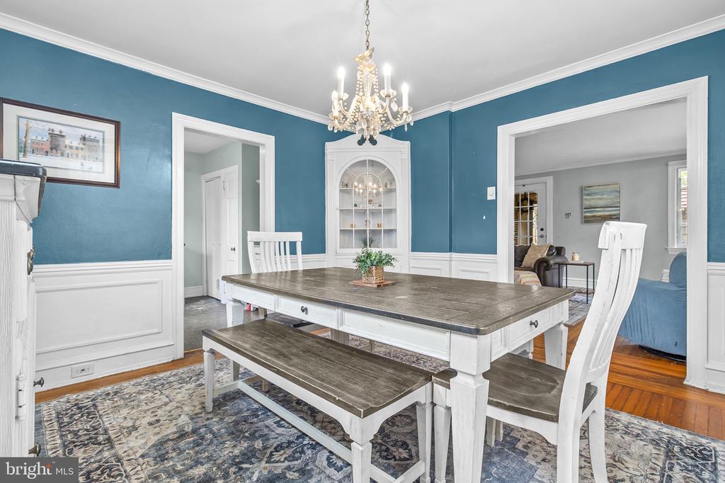 Dining room with teal walls, white wainscoting, a large table, and chandelier.