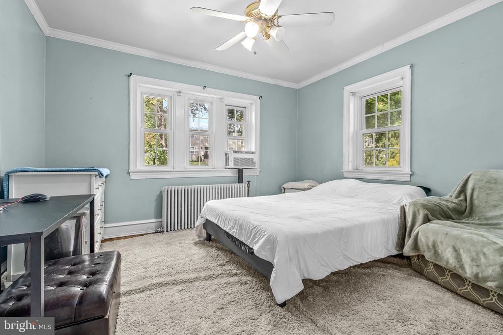 Bedroom with pale blue walls, a white bed, and windows above a radiator.