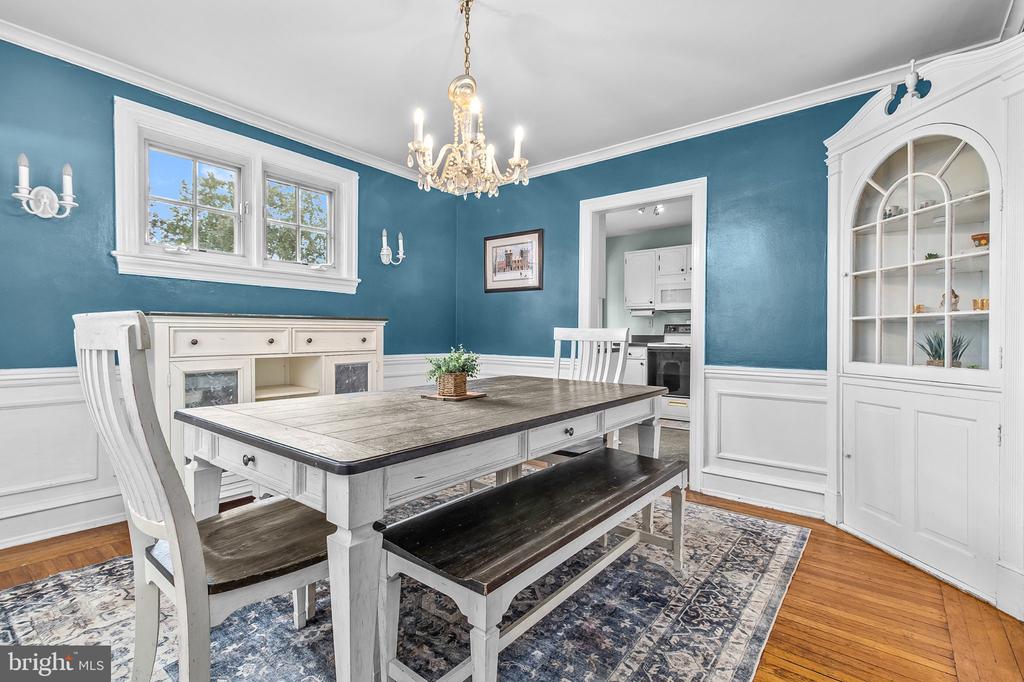 Dining room with teal walls, white wainscoting, a chandelier, and a large dining table.