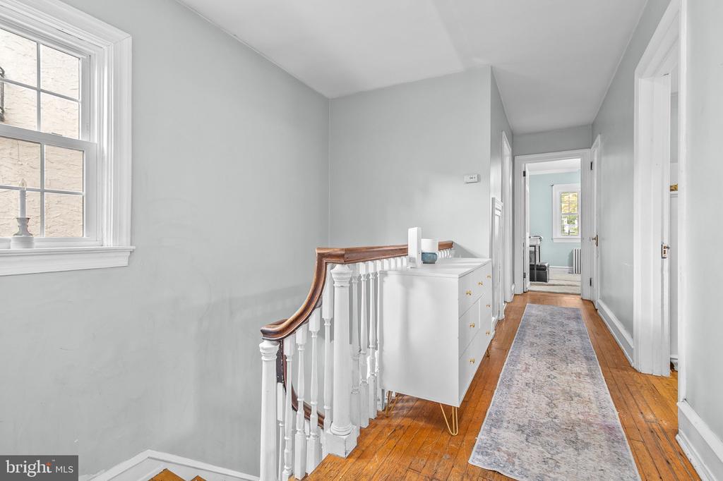 Hallway with hardwood floors, patterned runner, white console cabinet, and staircase with a wood handrail.