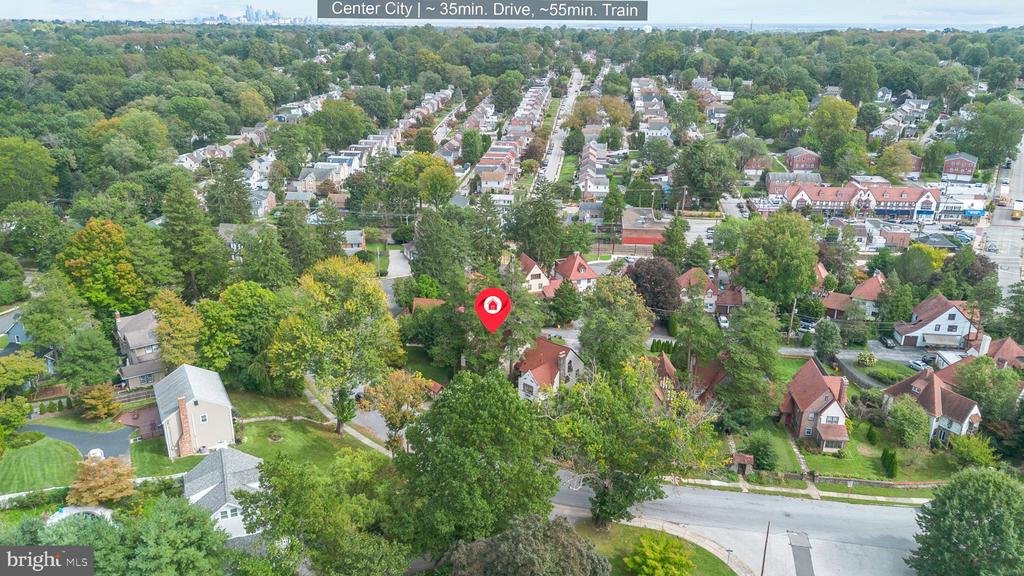 Aerial view of a leafy neighborhood with a red pin marking the property and a distant city skyline.