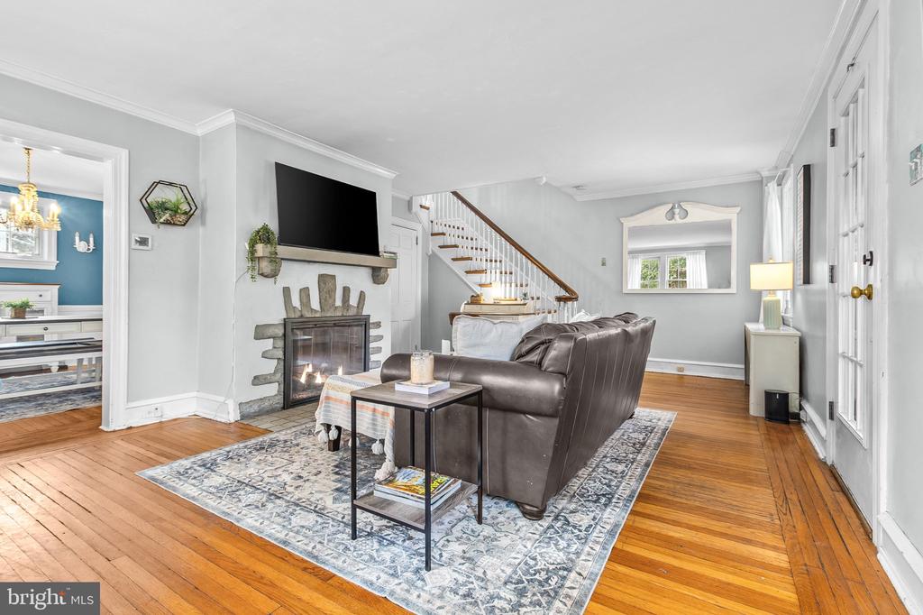 Furnished living room with a stone fireplace, brown leather sofa, hardwood floors, and staircase.