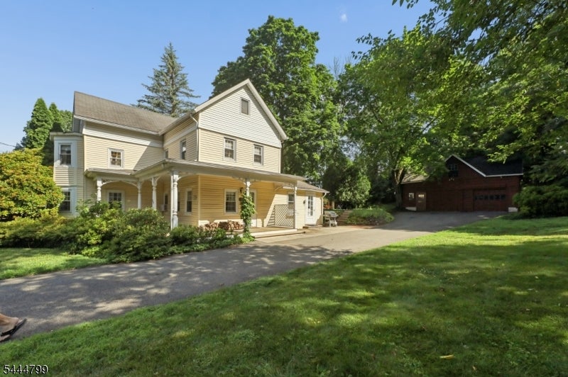 Light yellow two-story house with a covered porch, broad lawn, and detached garage.