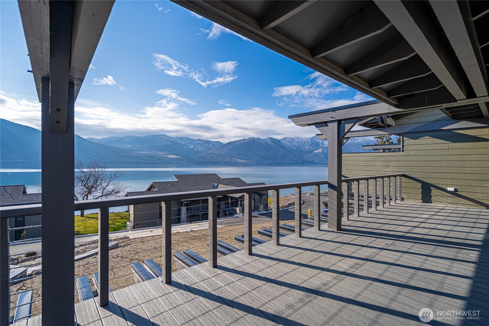 Covered deck overlooking a lake and mountain range, with neighboring homes below.