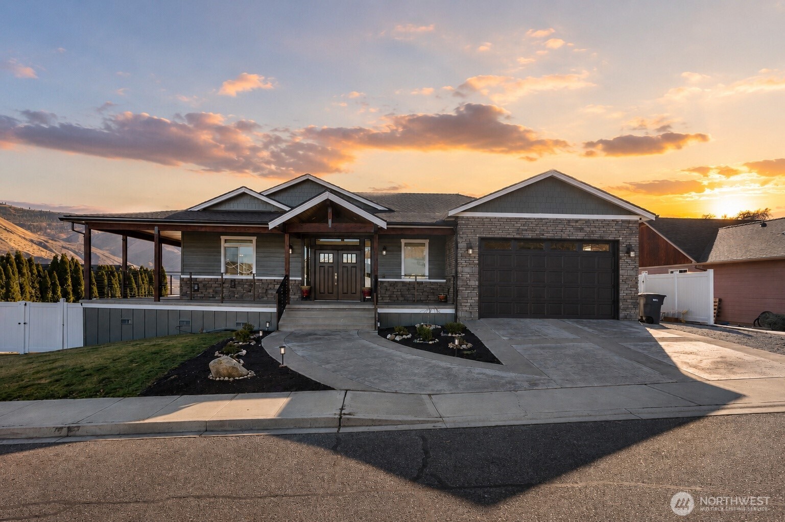 Single-story gray-and-stone house with a covered porch and double garage at sunset.