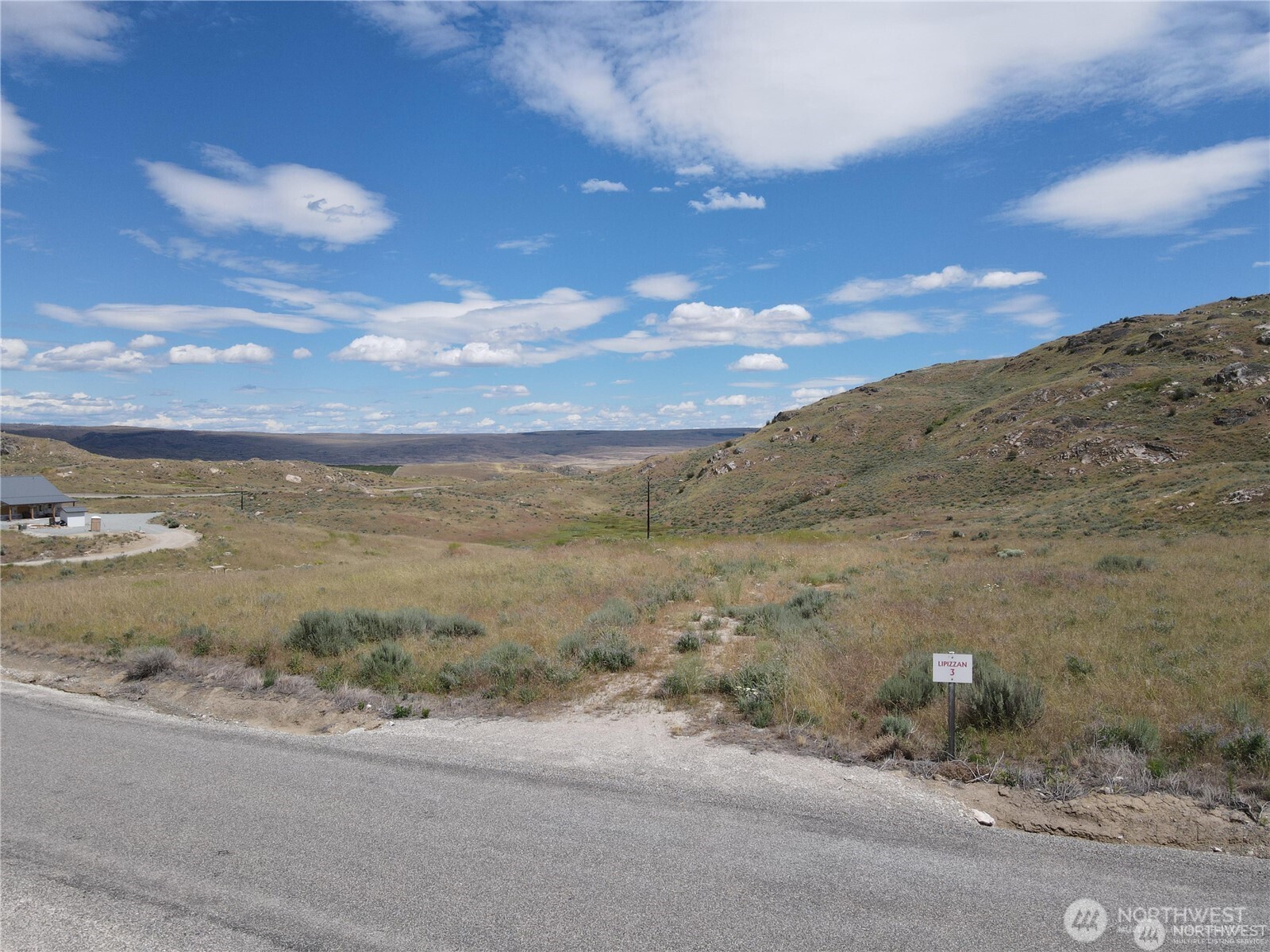 Vacant Lipizzan lot marked 3 beside a road, surrounded by dry grassland and rolling rocky hills.