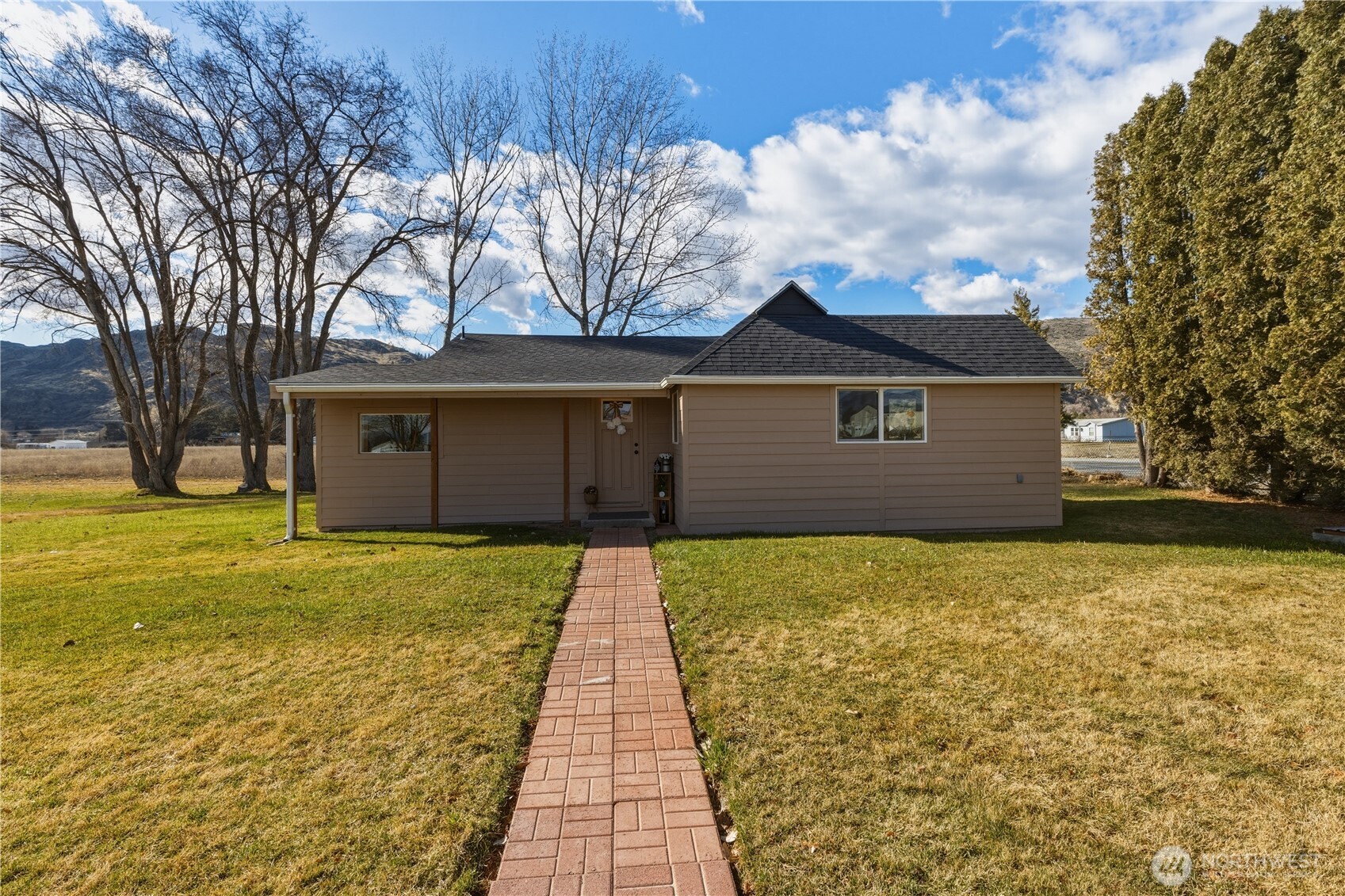Single-story tan house with a brick walkway, broad lawn, and mountains behind it.