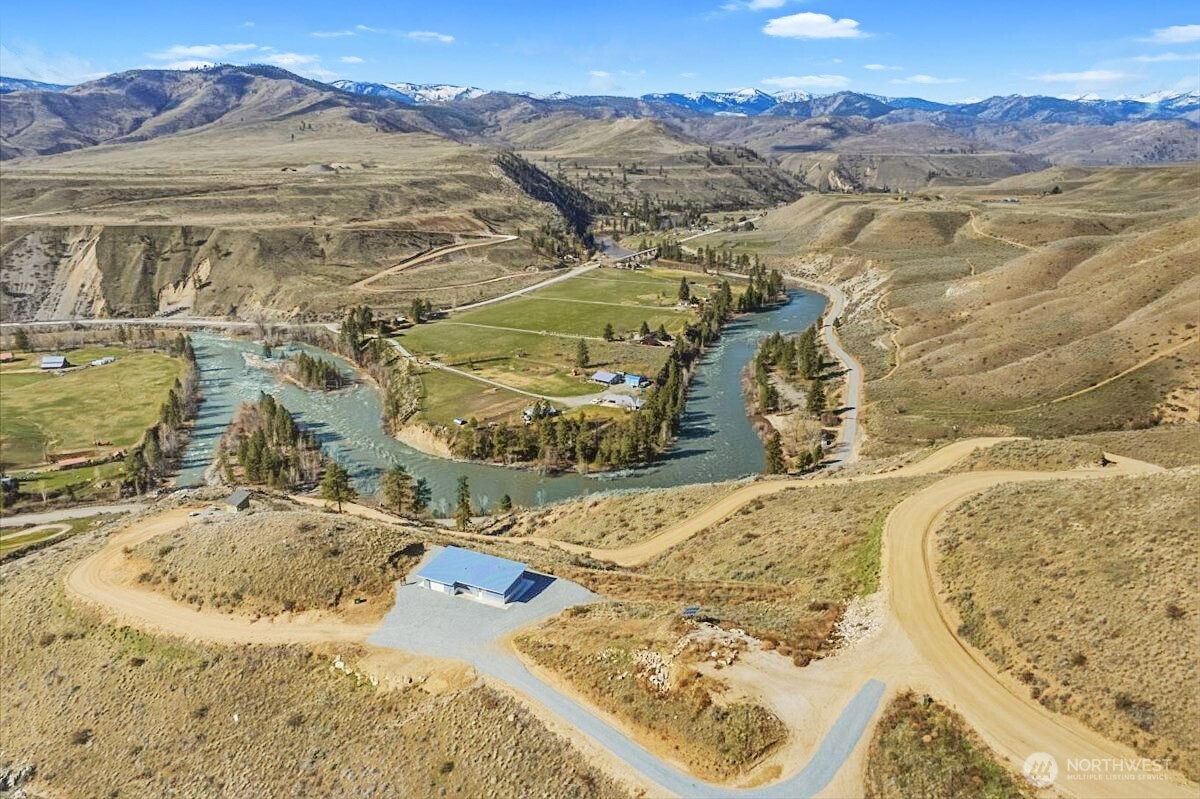 Aerial view of a river valley with waterways, winding dirt roads, and distant mountain ranges.