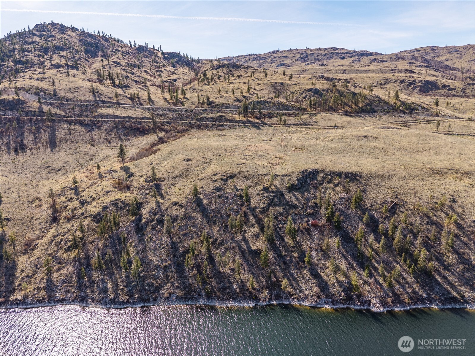 Aerial view of undeveloped riverfront land with dry rolling hills and sparse trees.