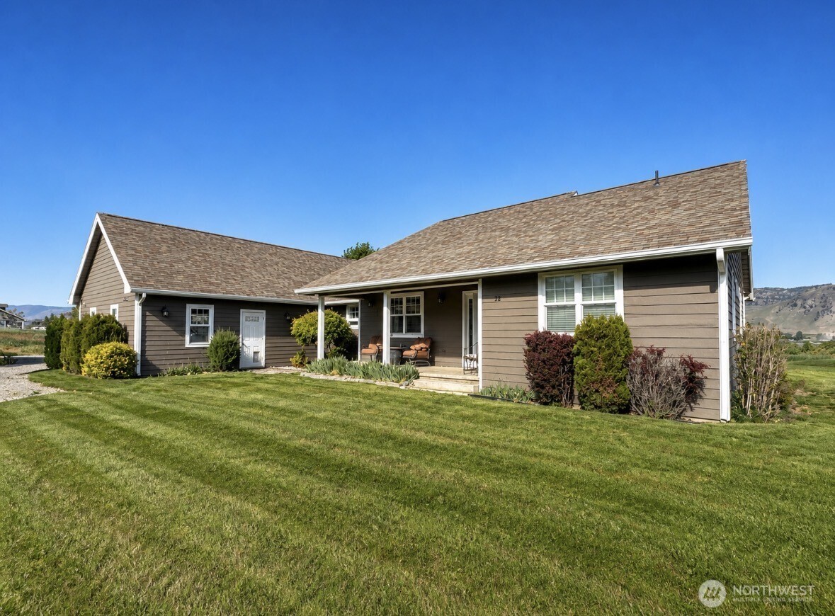 Single-story brown home with a covered porch, landscaped lawn, and distant hills.