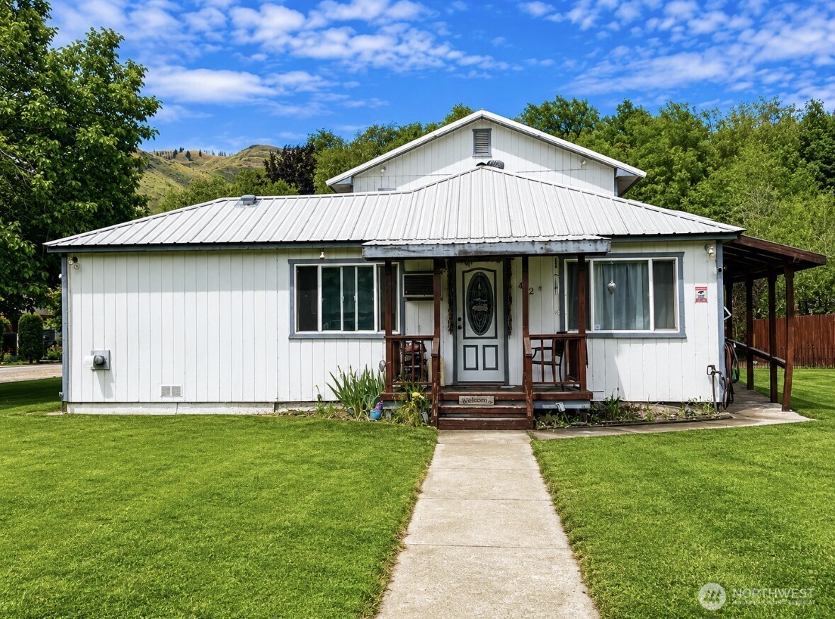 White single-story home with a metal roof, covered porch, and walkway across a green lawn.