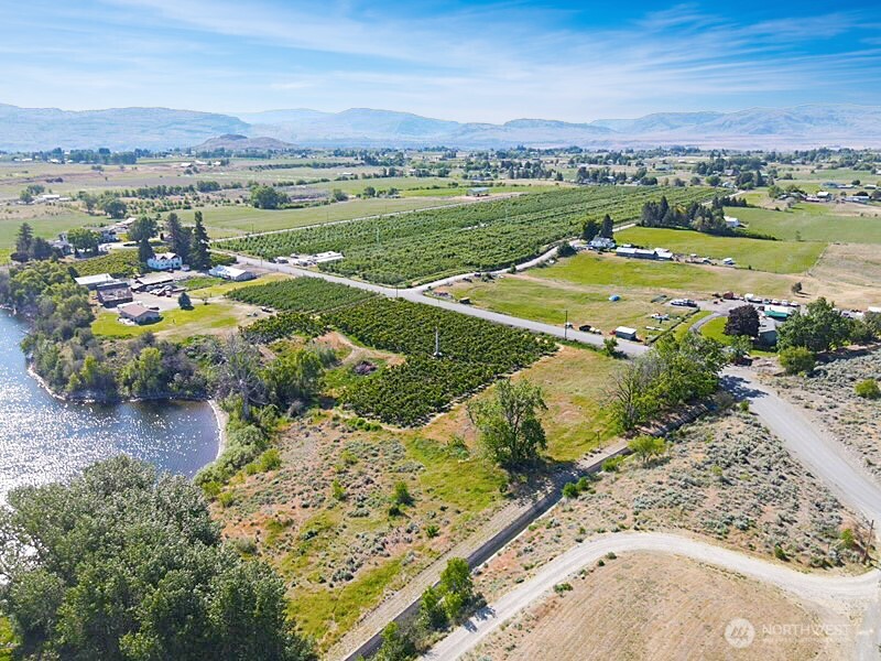 Aerial view of orchard rows and open fields beside water, with distant mountains.