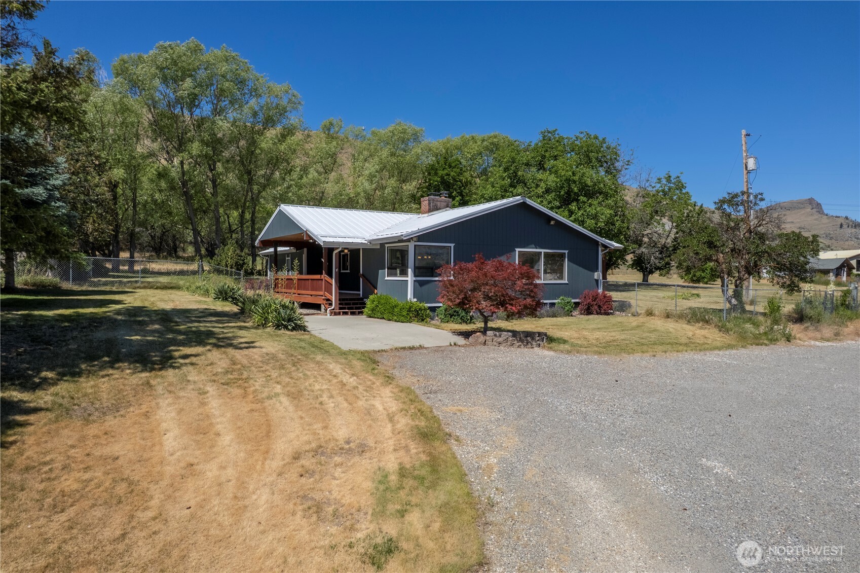 Dark blue single-story home with a metal roof, wooden porch, and gravel driveway.