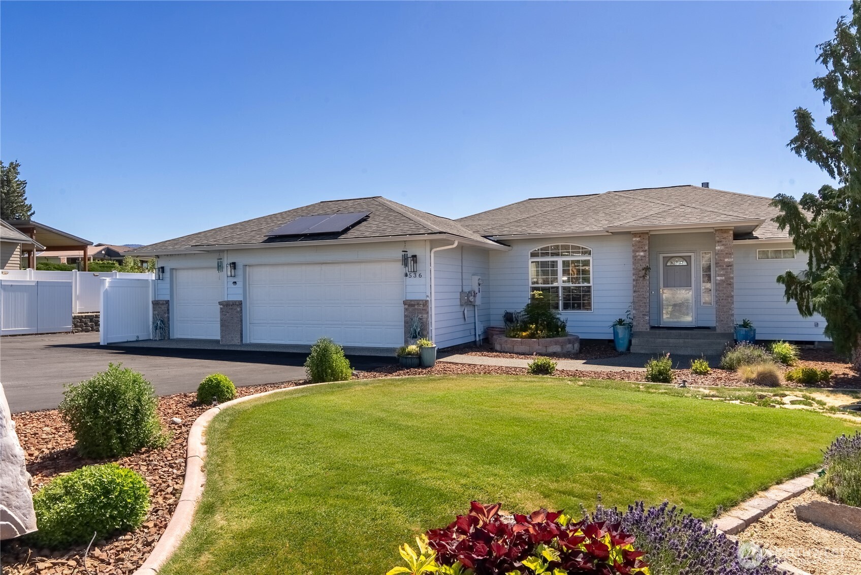 Light blue single-story home with rooftop solar panels, a two-car garage, and a landscaped front lawn.