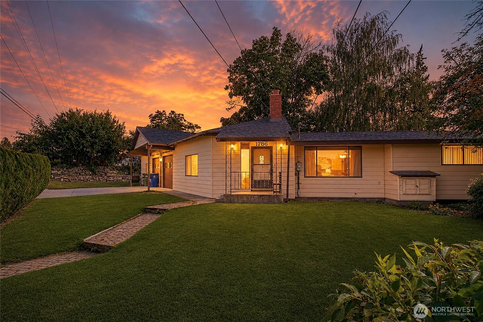 Single-story home at dusk with a lit covered entry and stone walkway across the lawn.