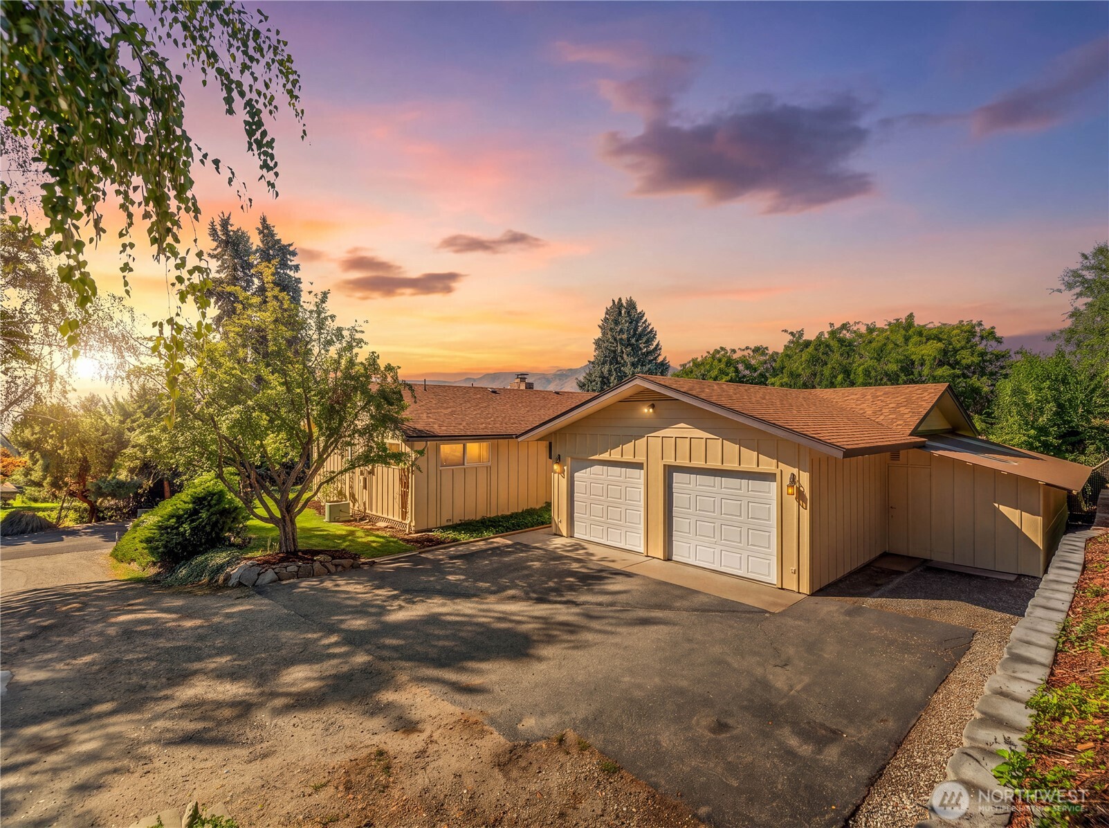 Tan single-story house with two white garage doors and a broad driveway at sunset.