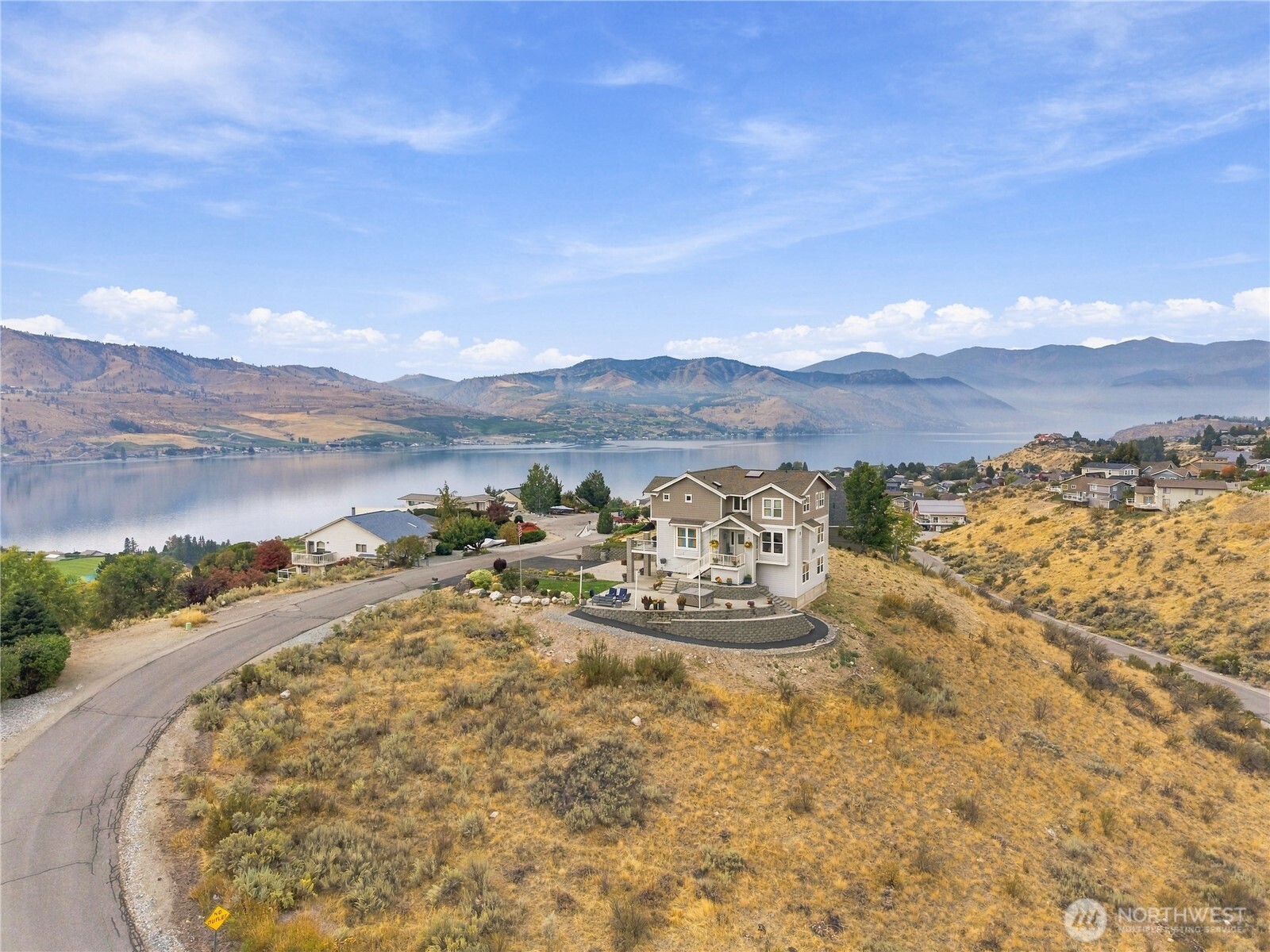 Two-story hillside home overlooking a lake, with mountain views.
