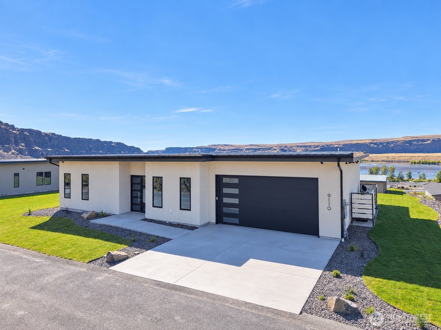 Modern single-story home with a dark garage door, landscaped lawn, and river canyon views.
