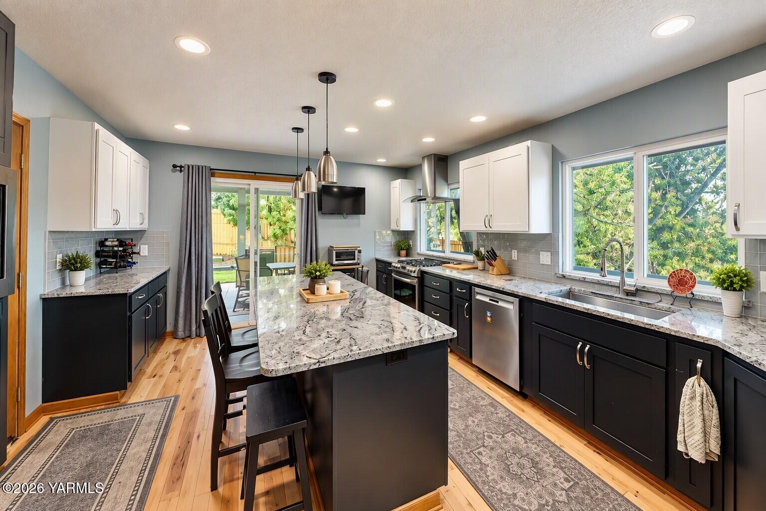 Kitchen with a large marble-pattern island, dark cabinets, and wide windows overlooking greenery.