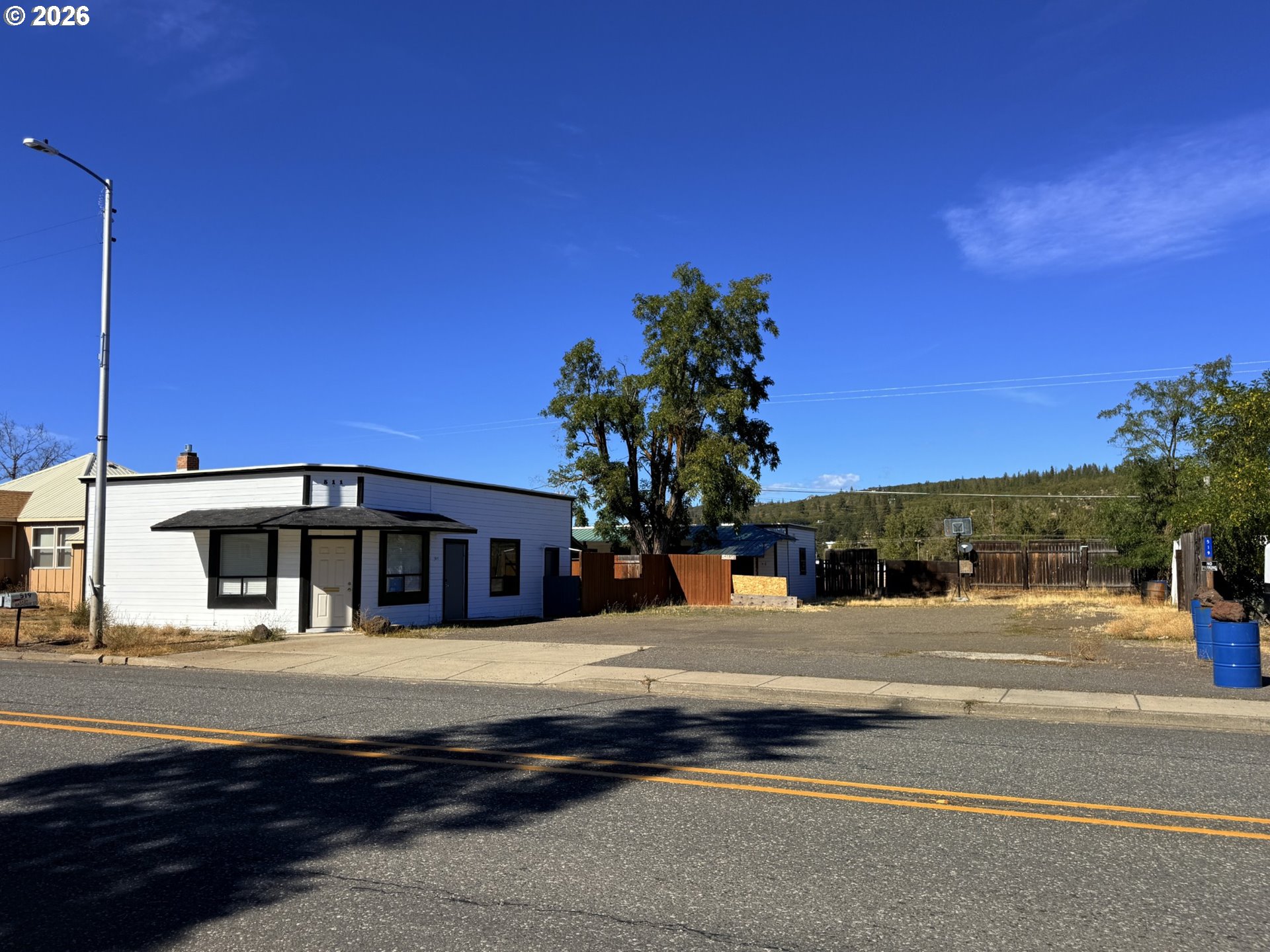 White single-story building with dark trim and a fenced paved lot along the street.