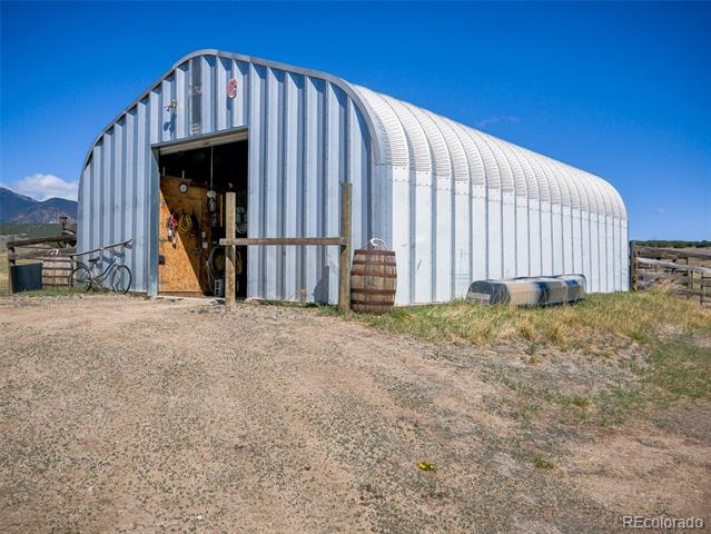 Silver arched metal barn with an open entrance, bicycle, and barrel outside.