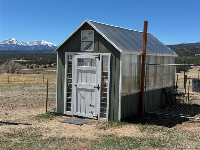 Gray gable-roofed shed with greenhouse panels, set against snow-capped mountains.