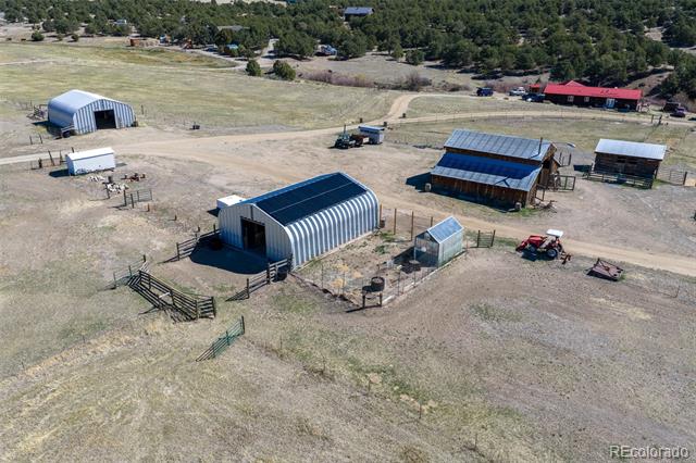 Aerial view of rural acreage with metal barns, fenced paddocks, and open fields.