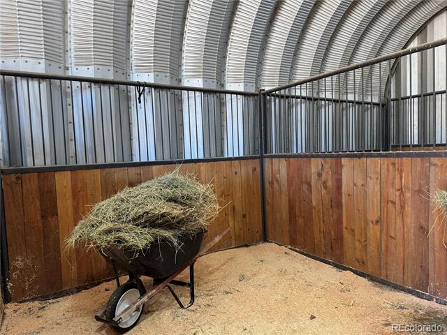 Interior horse stall with wooden walls, metal railings, and a hay-filled wheelbarrow.
