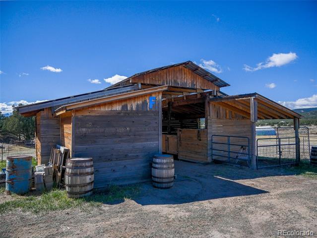 Rustic wooden barn with open stalls, metal corral fencing, and barrels in the yard.