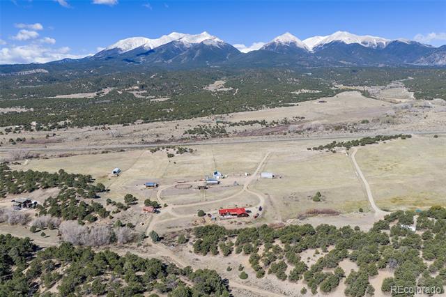 Rural property with scattered buildings and fields, backed by a panoramic range of snow-capped mountains.