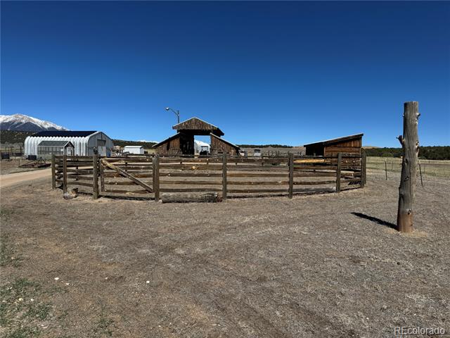 Rural ranch corral with wooden fencing, outbuildings, and snow-covered mountains in the distance.
