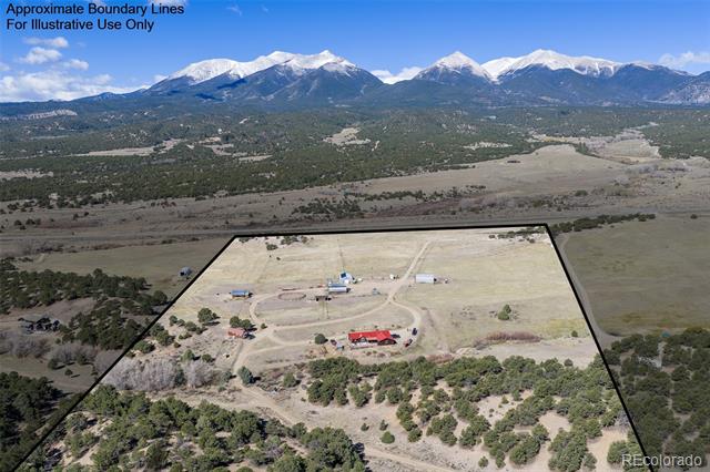 Aerial view of a rural property outlined against open fields, trees, and snow-capped mountains.