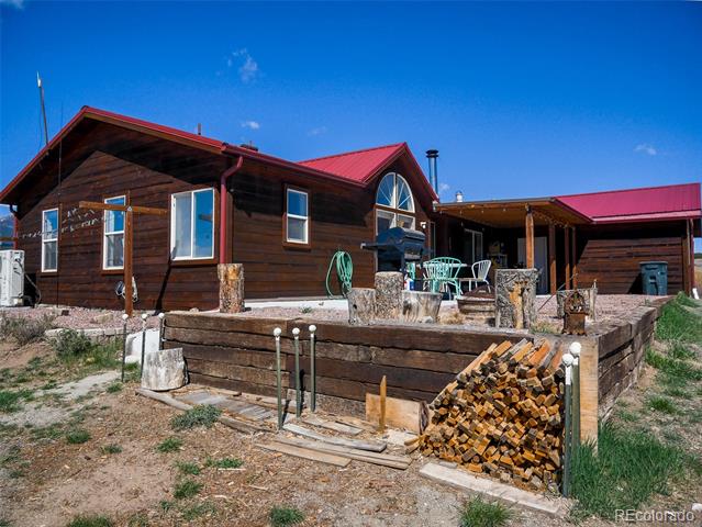 Dark wood house with red metal roofs, turquoise patio furniture, and stacked firewood.