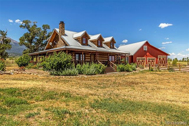 Rustic log home with a covered porch beside a red barn, with mountains in the distance.