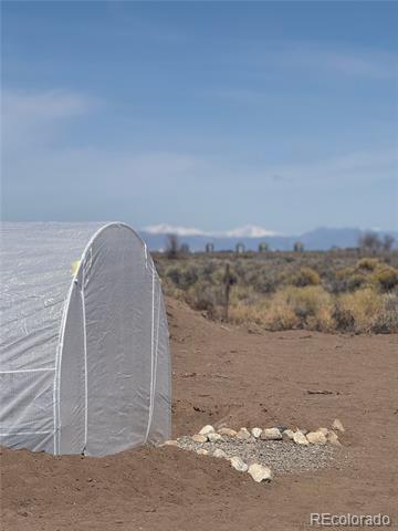 Rural land with a white hoop greenhouse, scrub vegetation, and distant mountains.