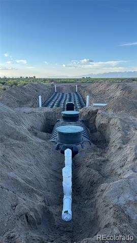 Septic system under construction, with black tanks and pipes exposed in a long trench.
