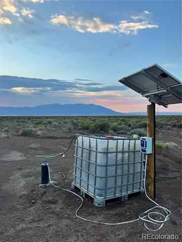 Water storage tank and solar-powered well on rural land, with distant mountains at dusk.