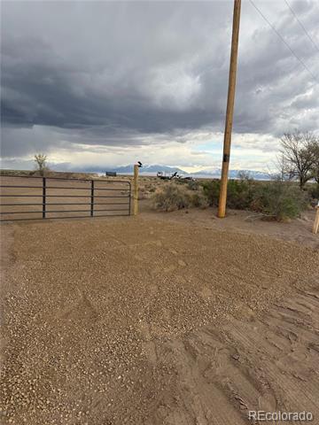 Gravel entrance to a rural property with a metal gate and distant mountains.
