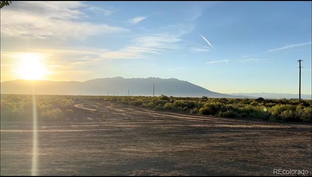 Rural vacant land with scrub, a mountain range, and warm sunset light.